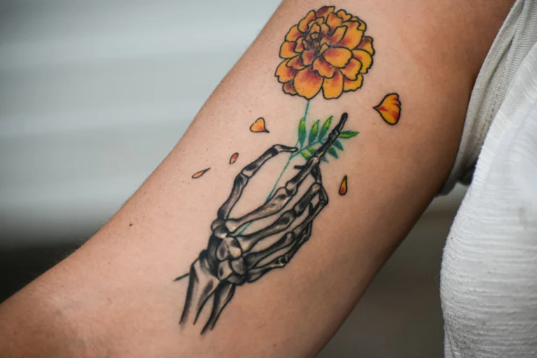 A hand holding a flower, tattooed on the arm